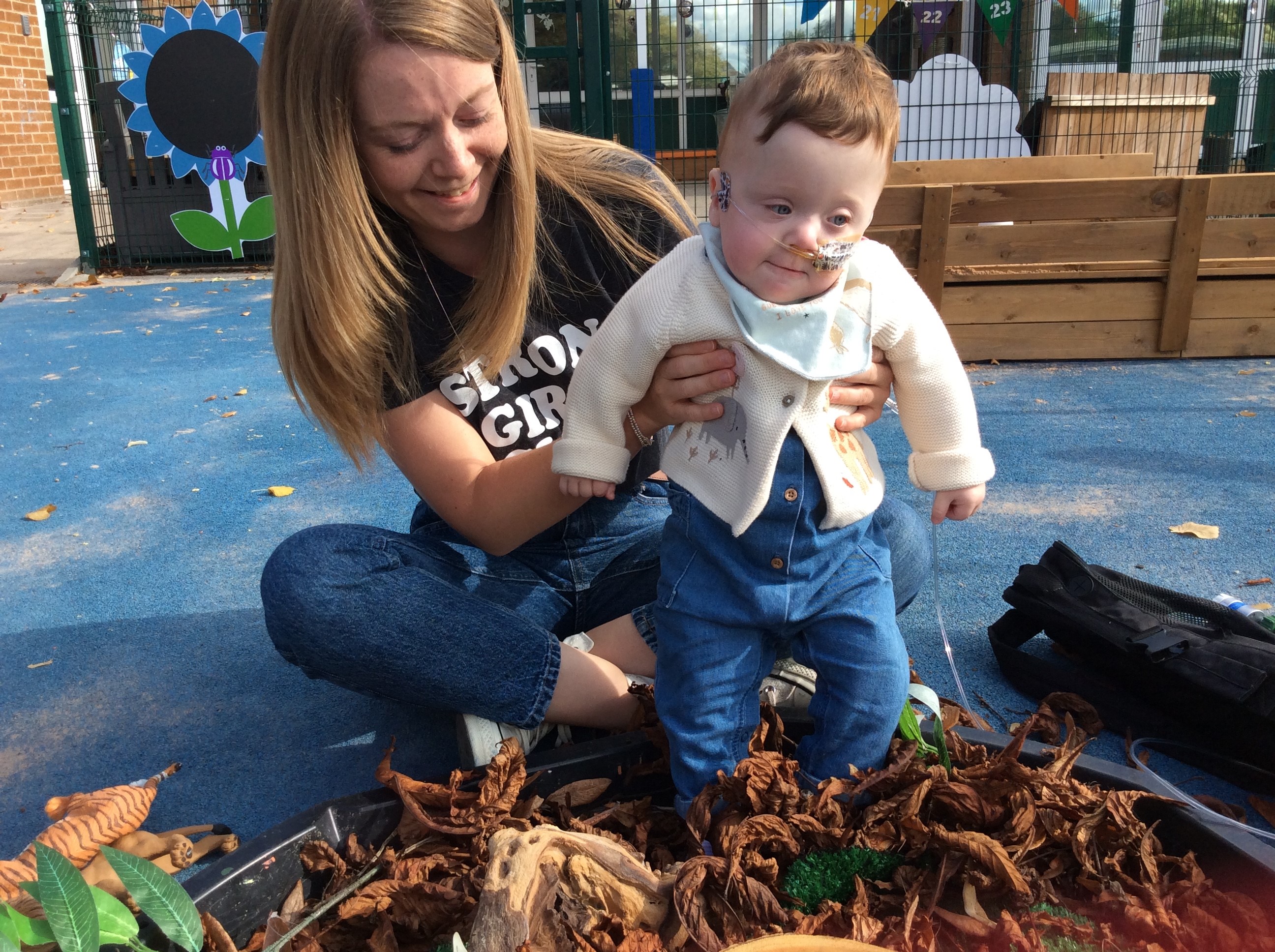 Young child being held by adult while kicking leaves outside