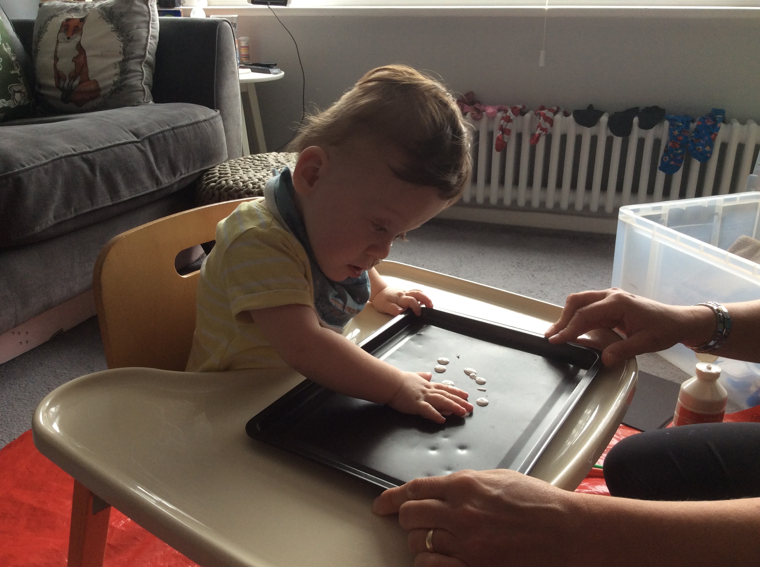 Young child using hands to swirl white paint on a tray