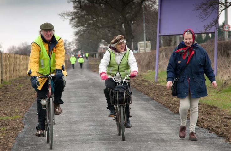 Couple enjoying leisurely cycle while chatting to person walking