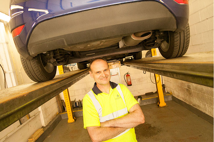 Vehicle tester stood in a testing pit under a car on ramp.